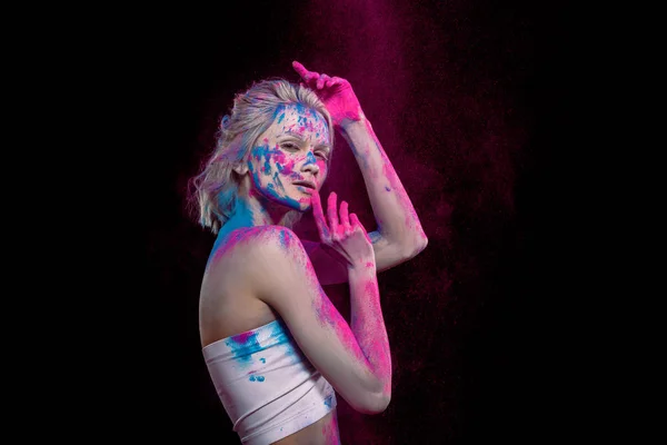 Jolie jeune femme posant en rose et bleu holi peinture, isolé sur noir — Photo de stock