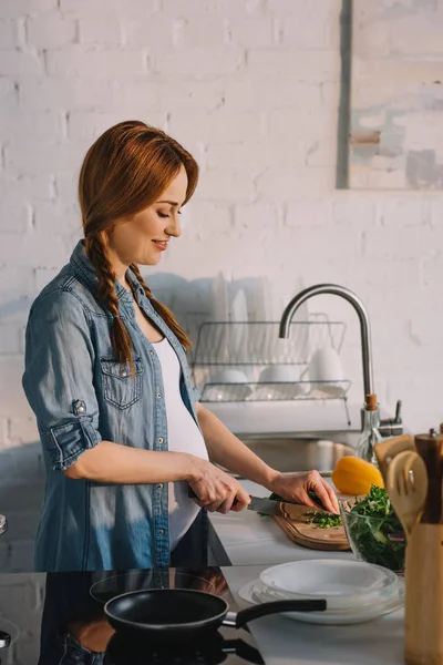 Side view of attractive pregnant woman preparing salad at kitchen — Stock Photo