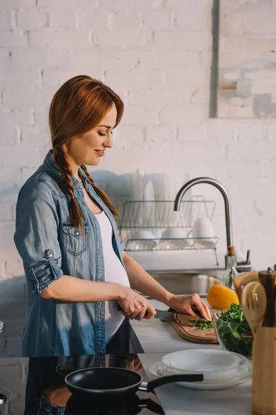 Vue latérale de la femme enceinte attrayante préparant la salade à la cuisine — Photo de stock