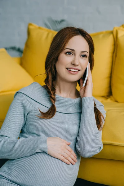 Atractiva mujer embarazada hablando por teléfono inteligente en la sala de estar - foto de stock