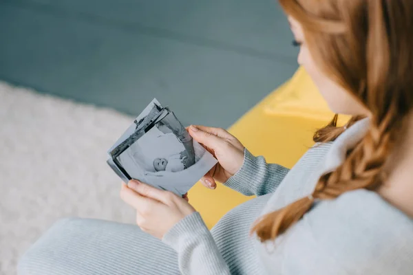 Обрізане зображення вагітної жінки, що тримає фото новонародженої дитини у вітальні — стокове фото