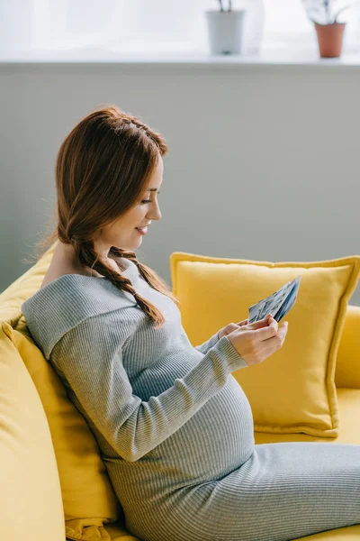 Vista laterale di attraente donna incinta guardando le foto in soggiorno — Foto stock