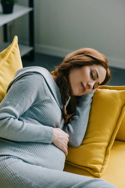 Séduisante femme enceinte dormant sur canapé dans le salon — Photo de stock