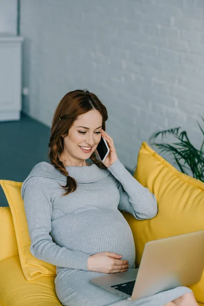 High angle view of attractive pregnant woman talking by smartphone and using laptop in living room — Stock Photo