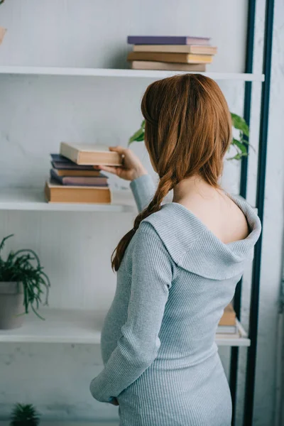 Side view of pregnant woman taking book from bookshelf at home — Stock Photo