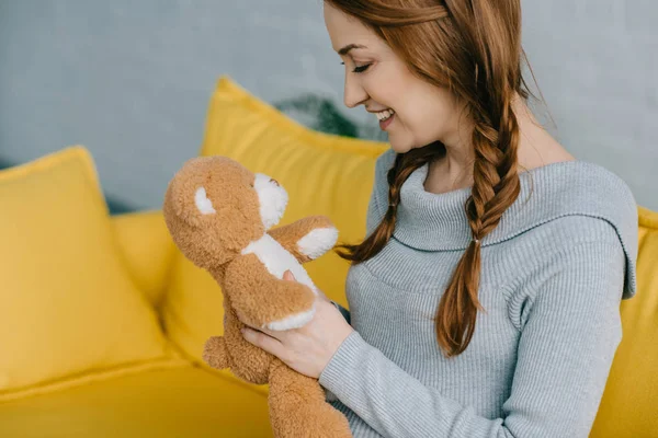 Side view of beautiful pregnant woman looking at teddy bear in living room — Stock Photo