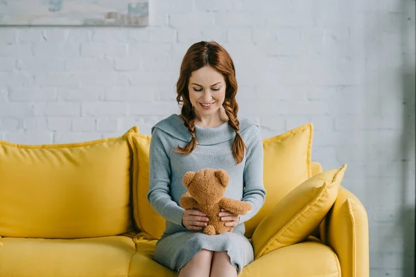 Beautiful pregnant woman sitting with teddy bear in living room — Stock Photo