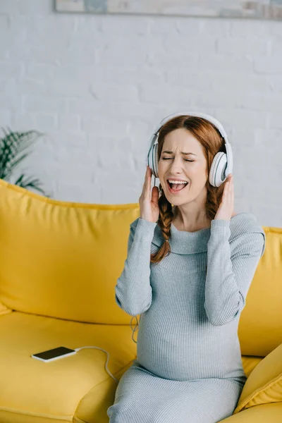 Felice donna incinta ascoltando musica e cantando in soggiorno — Foto stock