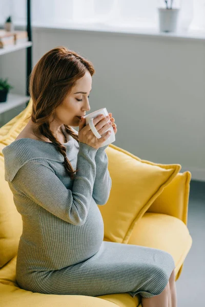 Side view of beautiful pregnant woman drinking tea in living room — Stock Photo