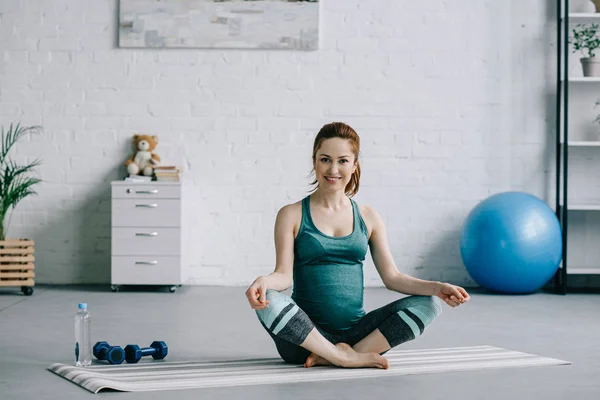 Beautiful pregnant woman sitting in lotus position in living room — Stock Photo