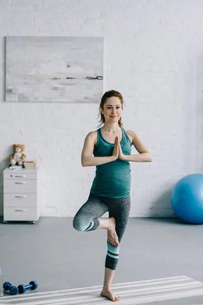Schöne schwangere Frau macht Yoga-Baumstellung im Wohnzimmer — Stockfoto