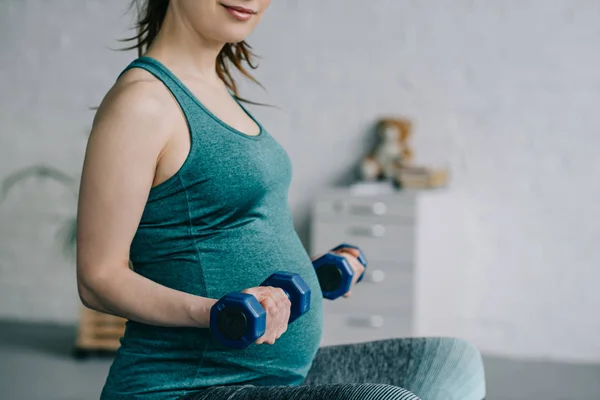 Immagine ritagliata della donna incinta che si esercita con i manubri a casa — Foto stock