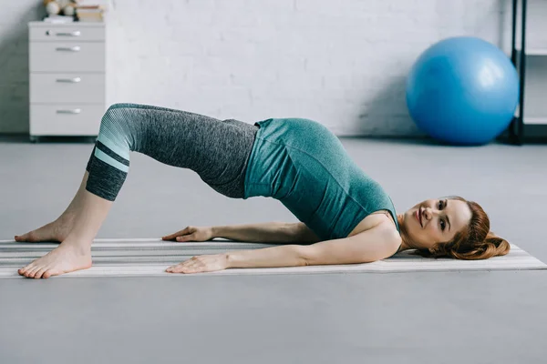 Bella donna incinta che esercita sul tappetino yoga in soggiorno — Foto stock