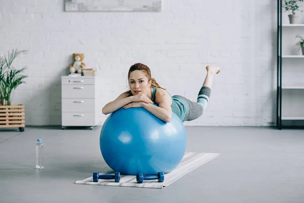 Hermosa mujer embarazada haciendo ejercicio en la pelota de fitness en la sala de estar - foto de stock