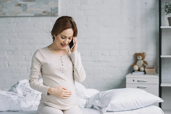 Hermosa mujer embarazada hablando por teléfono inteligente en el dormitorio - foto de stock
