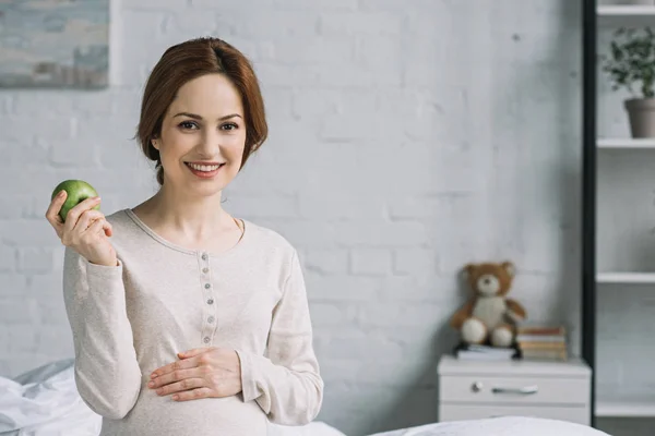 Attraktive Schwangere sitzt mit reifem Apfel im Bett — Stockfoto