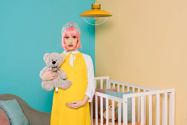 Style rétro pin up enceinte femme avec des cheveux roses tenant ours en peluche dans la chambre d'enfant — Photo de stock