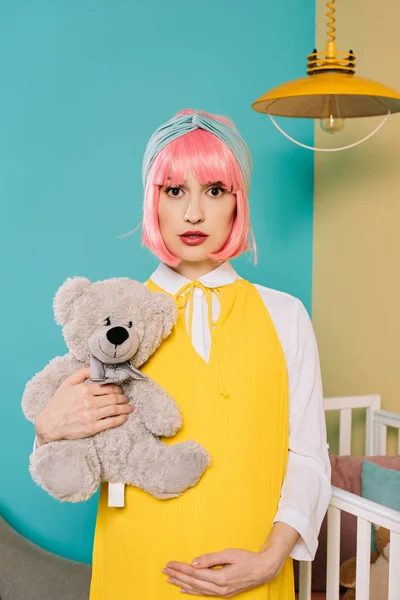 Portrait de femme enceinte style rétro pin up avec des cheveux roses tenant ours en peluche dans la chambre d'enfant — Photo de stock