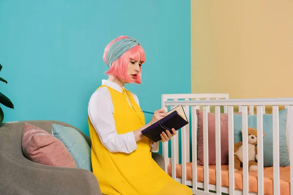 Mujer embarazada estilo retro pin up con pelo rosa escribir algo para portátil en la habitación de los niños - foto de stock
