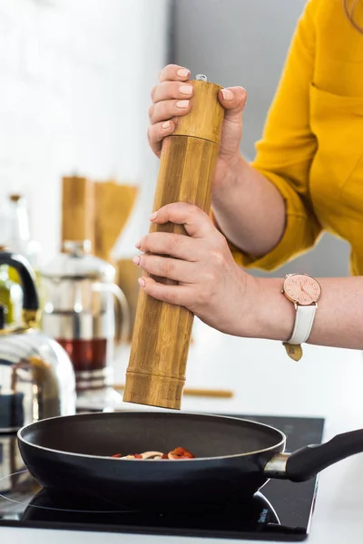 Immagine ritagliata di donna che aggiunge spezie a frittura di verdure a cucina — Foto stock