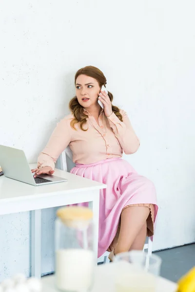 Schöne Frau, die mit Smartphone und Laptop in der Küche spricht — Stockfoto