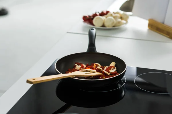 Frying pan with delicious vegetables on electric stove in kitchen — Stock Photo