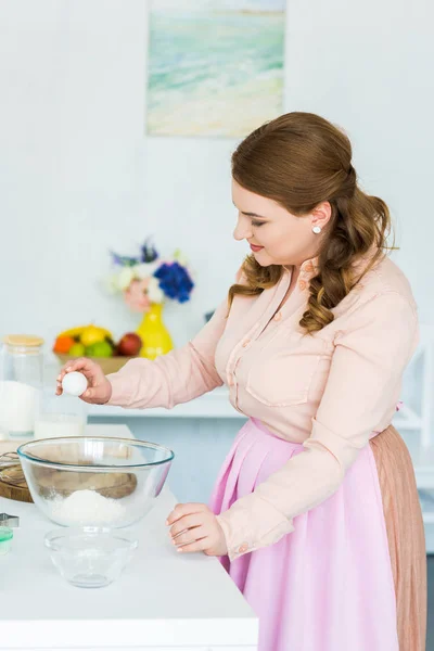 Vue latérale de belle femme cassant oeuf pour la pâte dans la cuisine — Photo de stock
