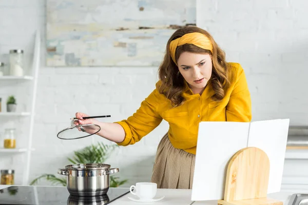 Beautiful woman cooking and reading recipe book in kitchen — Stock Photo