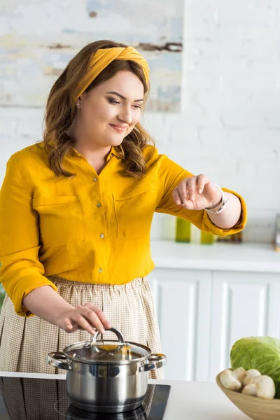Attraktive Frau überprüft Zeit auf Armbanduhr in der Nähe Pfanne auf Elektroherd in Küche — Stockfoto