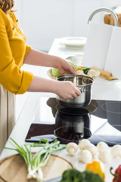 Imagen recortada de la mujer poniendo la cacerola en la cocina eléctrica - foto de stock