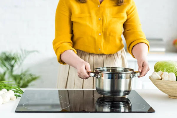 Imagem cortada de mulher colocando panela no fogão elétrico na cozinha — Fotografia de Stock