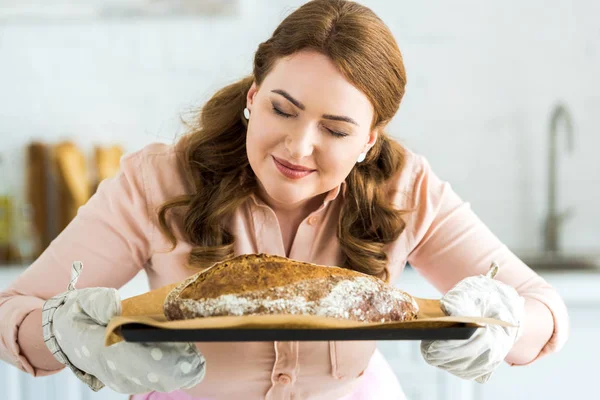 Beautiful woman sniffing homemade loaf of bread at kitchen — Stock Photo