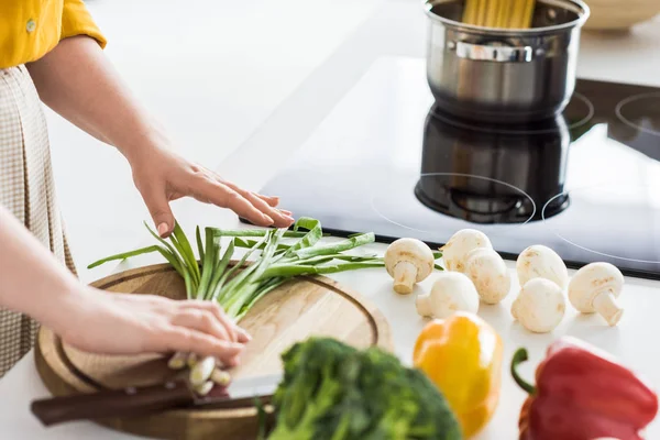 Image recadrée de femme mettant l'oignon vert sur la planche à découper à la cuisine — Photo de stock