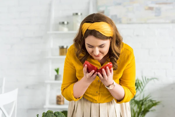 Beautiful woman sniffing ripe red bell pepper at kitchen — Stock Photo