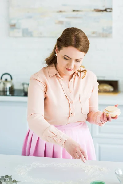 Schöne Frau streut Mehl auf Küchentheke — Stockfoto