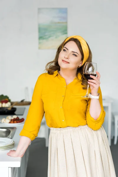 Весела красива жінка тримає келих вина і дивиться на кухню — стокове фото