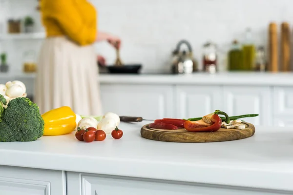 Imagem cortada de mulher cozinhar na cozinha com legumes em primeiro plano — Fotografia de Stock