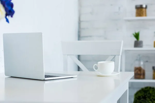 Laptop e xícara de café na cozinha da mesa branca — Fotografia de Stock