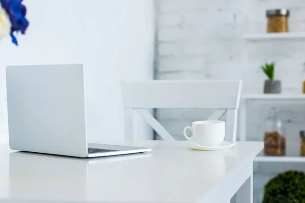 Portátil y taza de café en la cocina de mesa blanca - foto de stock