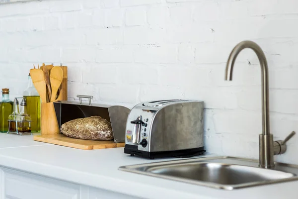 Tostadora, cesta de pan con pan cerca del lavabo en la cocina - foto de stock