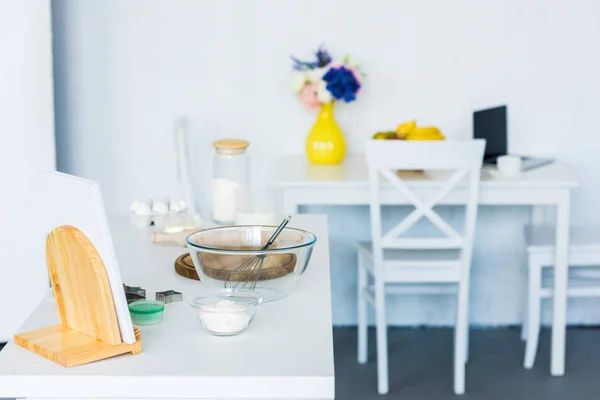 Bowl with whisk on kitchen counter, kitchen table with laptop — Stock Photo