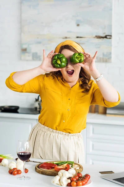 Hermosa mujer cubriendo los ojos con pimientos en la cocina - foto de stock