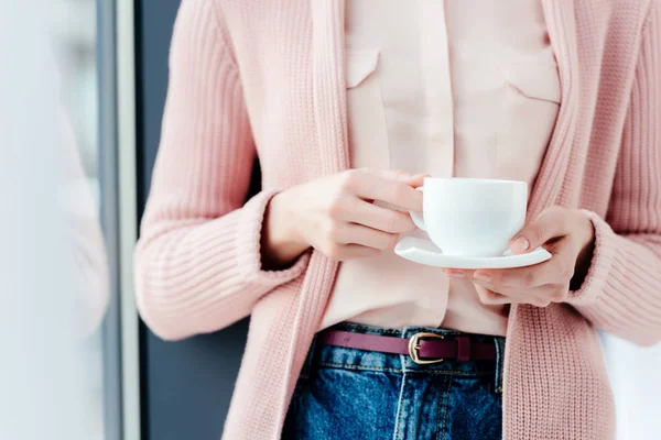 Partial view of woman in pink blouse and jeans with cup of coffee in hands — Stock Photo