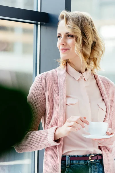 Donna pensierosa con una tazza di caffè che guarda fuori dalla finestra — Foto stock