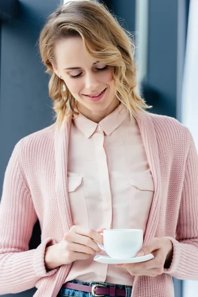 Porträt einer lächelnden Frau, die eine Tasse Kaffee in der Hand betrachtet — Stockfoto