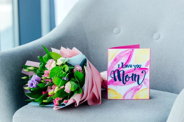 Primer plano vista de ramo envuelto de flores y te amo mamá felicitación postal en sillón, concepto de día de las madres - foto de stock