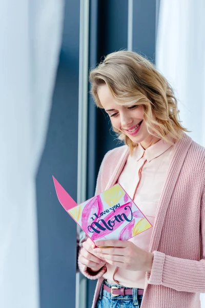 Smiling woman reading i love you mom postcard in hands, mothers day holiday concept — Stock Photo