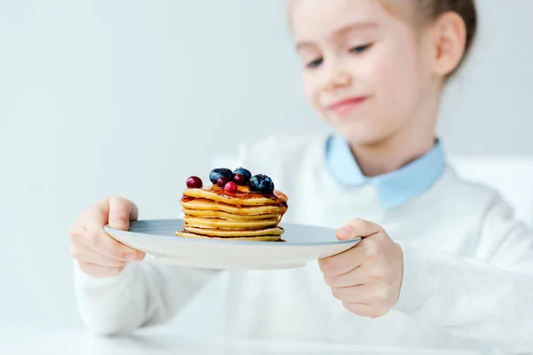 Selective focus of little kid looking at homemade pancakes with berries and honey in hands — Stock Photo