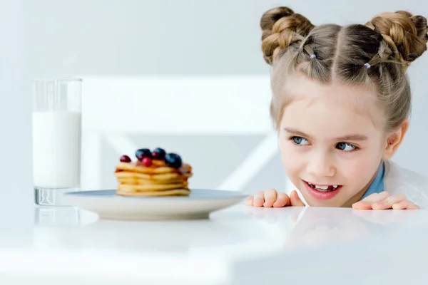 Foyer sélectif de petit enfant regardant des crêpes maison avec des baies et du miel sur la table — Photo de stock