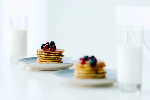 Selective focus of homemade pancakes with berries and honey and glasses of milk on tabletop — Stock Photo